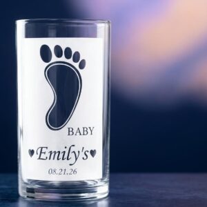 Clear glass vase with a frosted band showing a baby footprint, "Baby," the sample name "Emily's" and the date "08.21.26," against a blurred purple and blue background